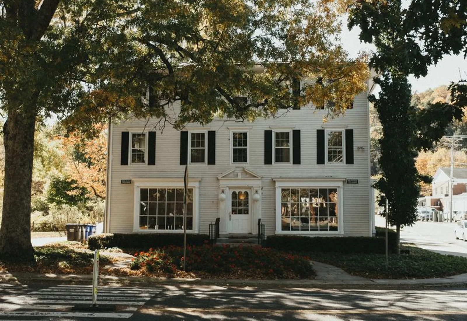The white clapboard house with black shutters behind autumn trees