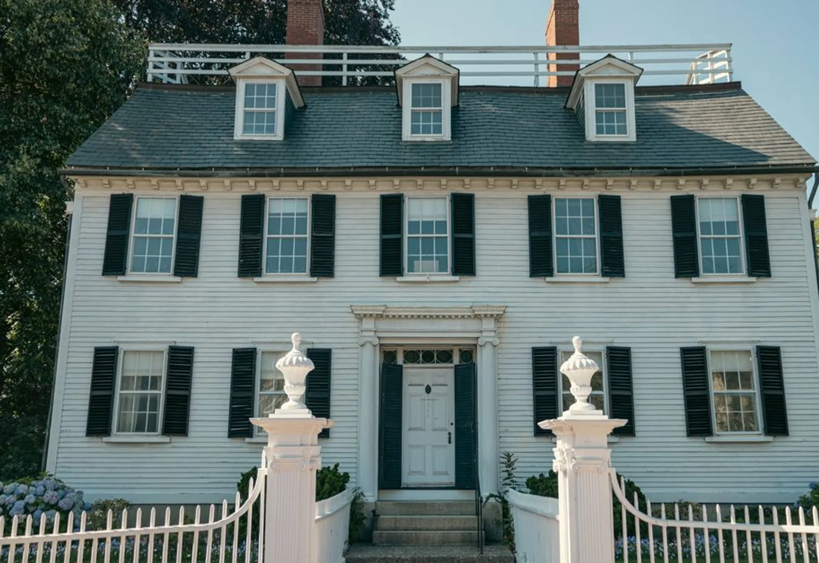 The white clapboard house behind its picket fence, windows lit at dusk