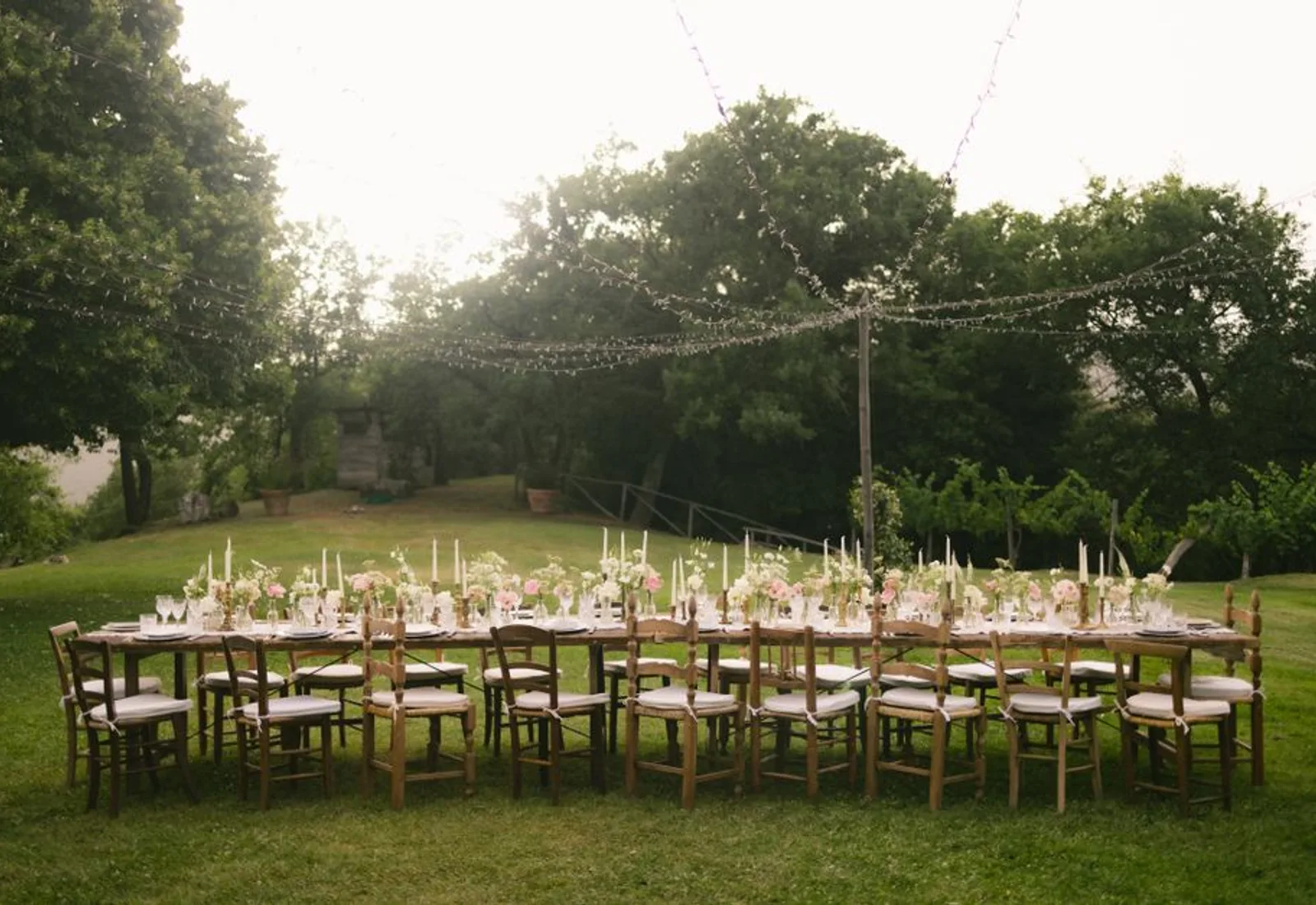 Long tables on the lawn under string lights, the harbor beyond