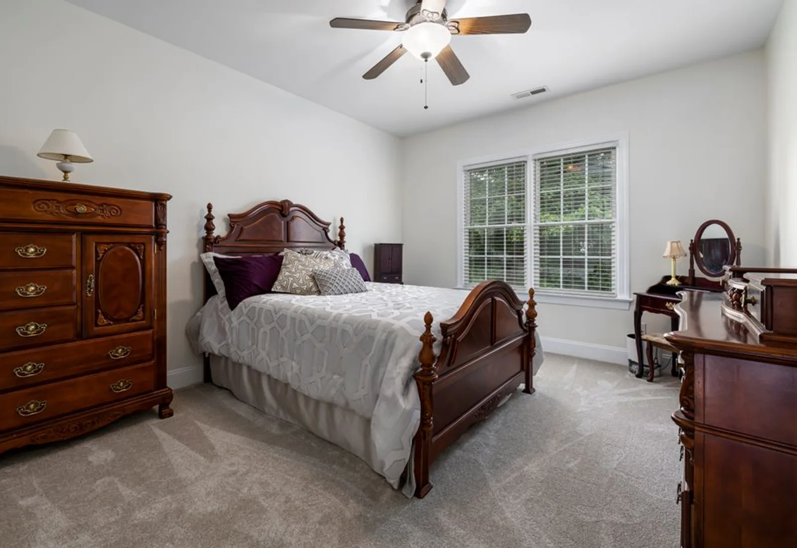 A king bed with an antique headboard, dresser and bright windows