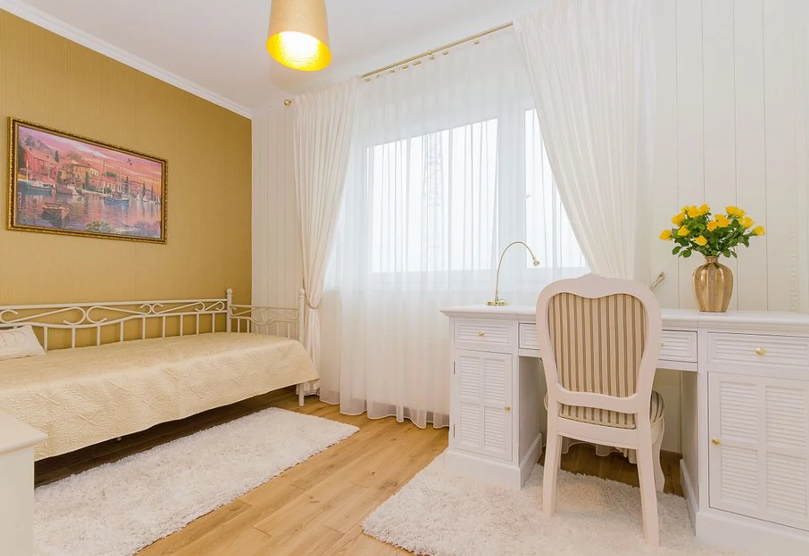 A queen bed beside a white writing desk under a curtained window