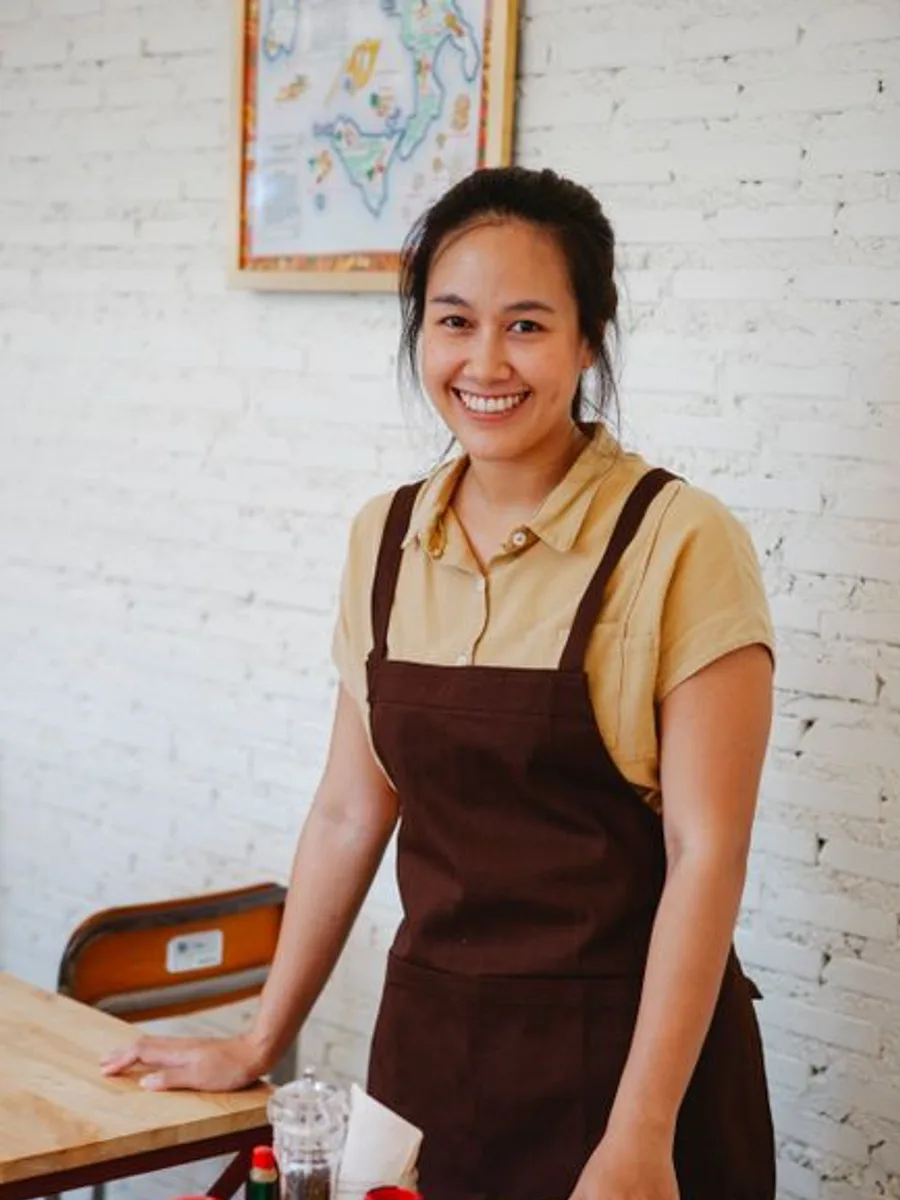 Nora, innkeeper, in an apron by a white wall
